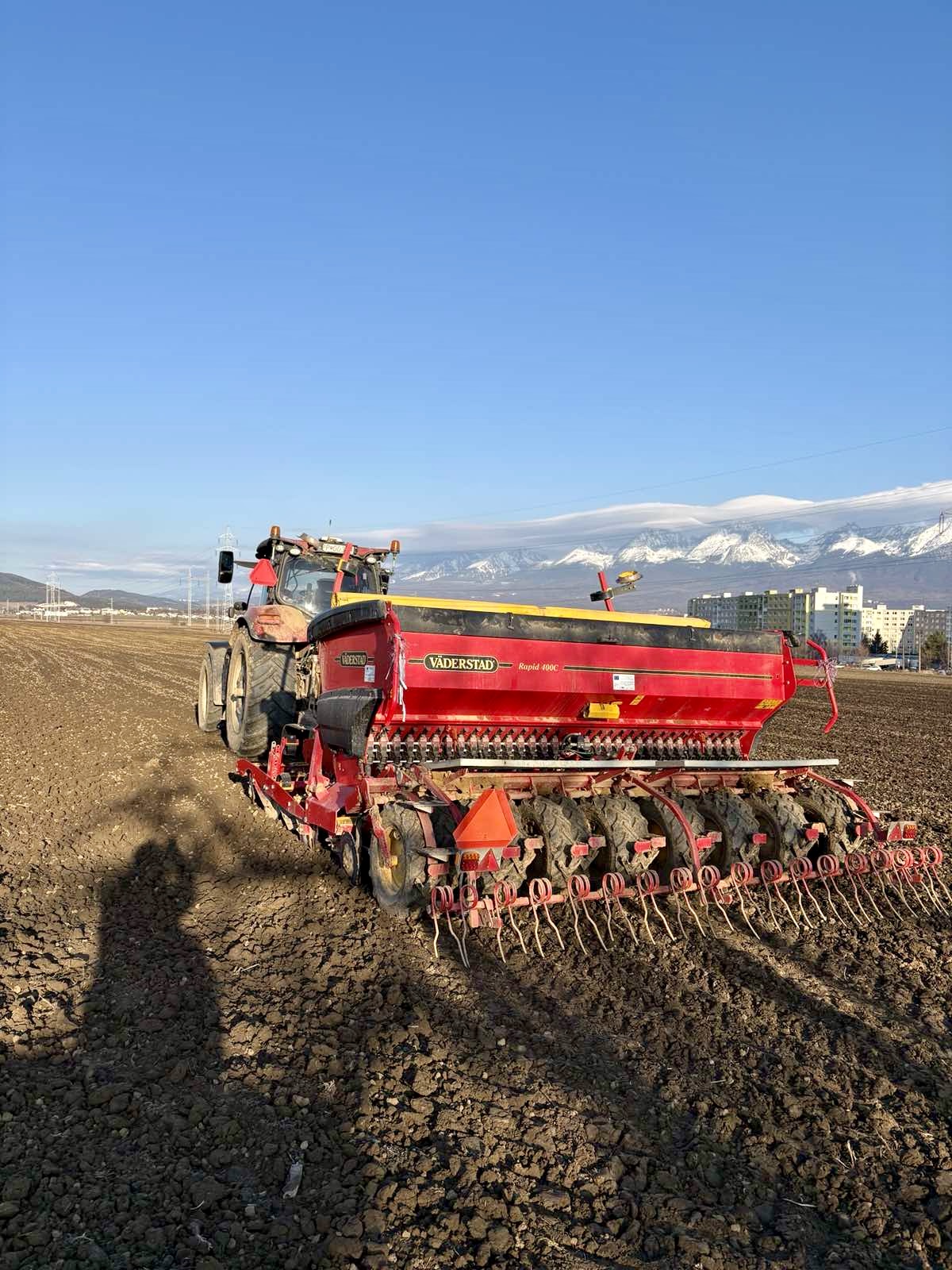 Traktor so sejačkou Väderstad Rapid 400C pri sejbe na zoranom poli s výhľadom na zasnežené Vysoké Tatry